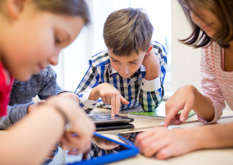 Close up of group of students standing around a shared table working on iPads