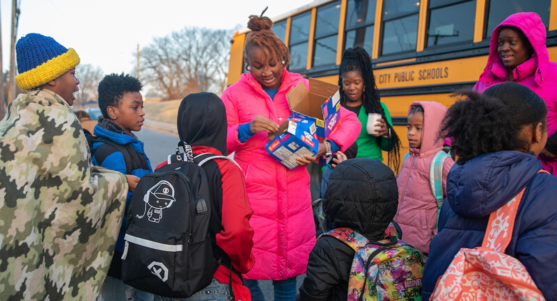 A family liaison shares breakfast snacks and words of encouragement with students getting off the bus at Martin Luther King Jr. Middle School.