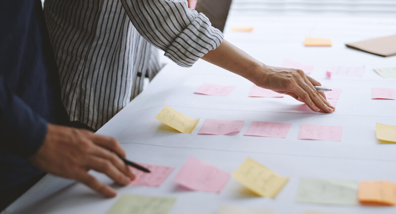 People reach out to pick up and set down different colored sticky notes which have placed on a table