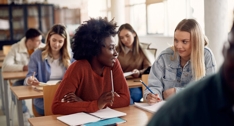 Two high school students sitting at a classroom table, engaged in a turn-and-talk conversation about the lesson