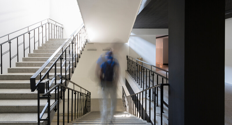 Photograph of a student walking down a stairwell, his body blurred to symbolize the idea of "absence" 