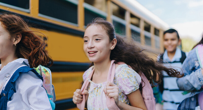 Children exit a bus and run happily toward school