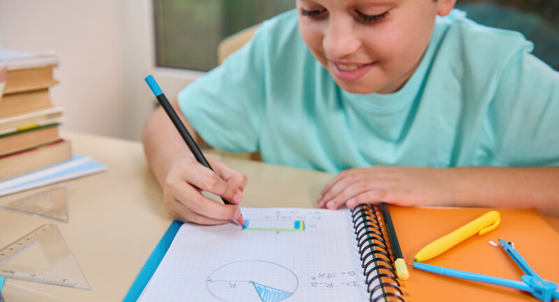 Student works on math calculations at a desk, smiling happily and confidently 