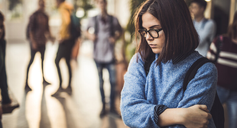 Photo of a female student in a crowded school hallway looking isolated and sad