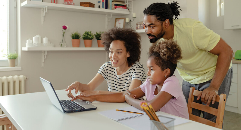 Photo of parents helping a young girl use a laptop.